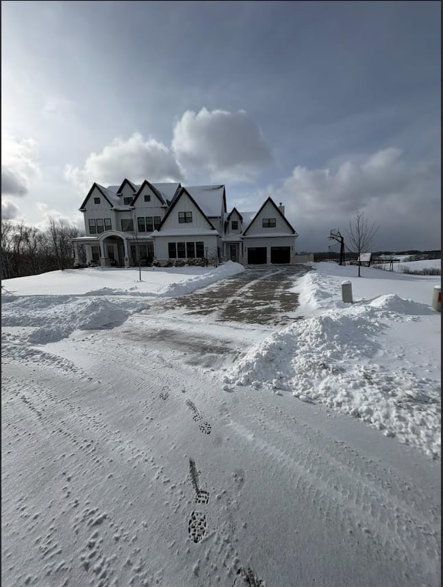 Large white two-story house with multiple gables surrounded by snow-covered landscape and cloudy winter sky