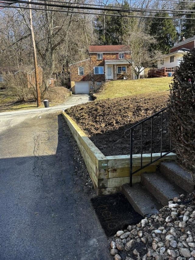 Brick house with raised garden bed in foreground, driveway, bare trees, and neighboring properties on residential street