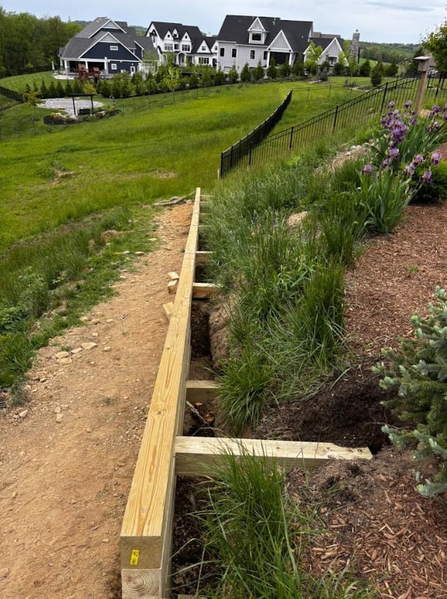 Wooden raised garden beds with purple flowers and plants in a landscaped yard with large houses in background