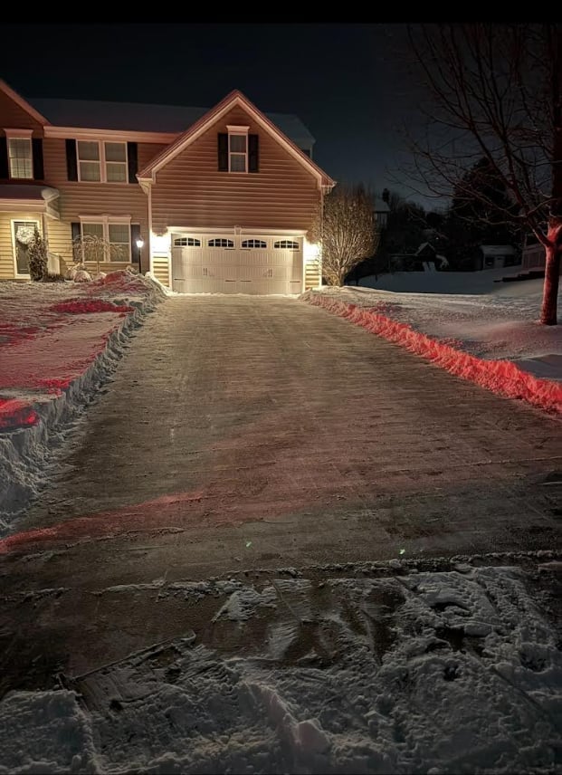 Two-story suburban home at night with illuminated driveway and garage door, decorated with red holiday lights along the borders