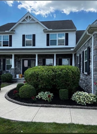 Two-story white house with black shutters, front porch, and landscaped front yard featuring green hedges and shrubs