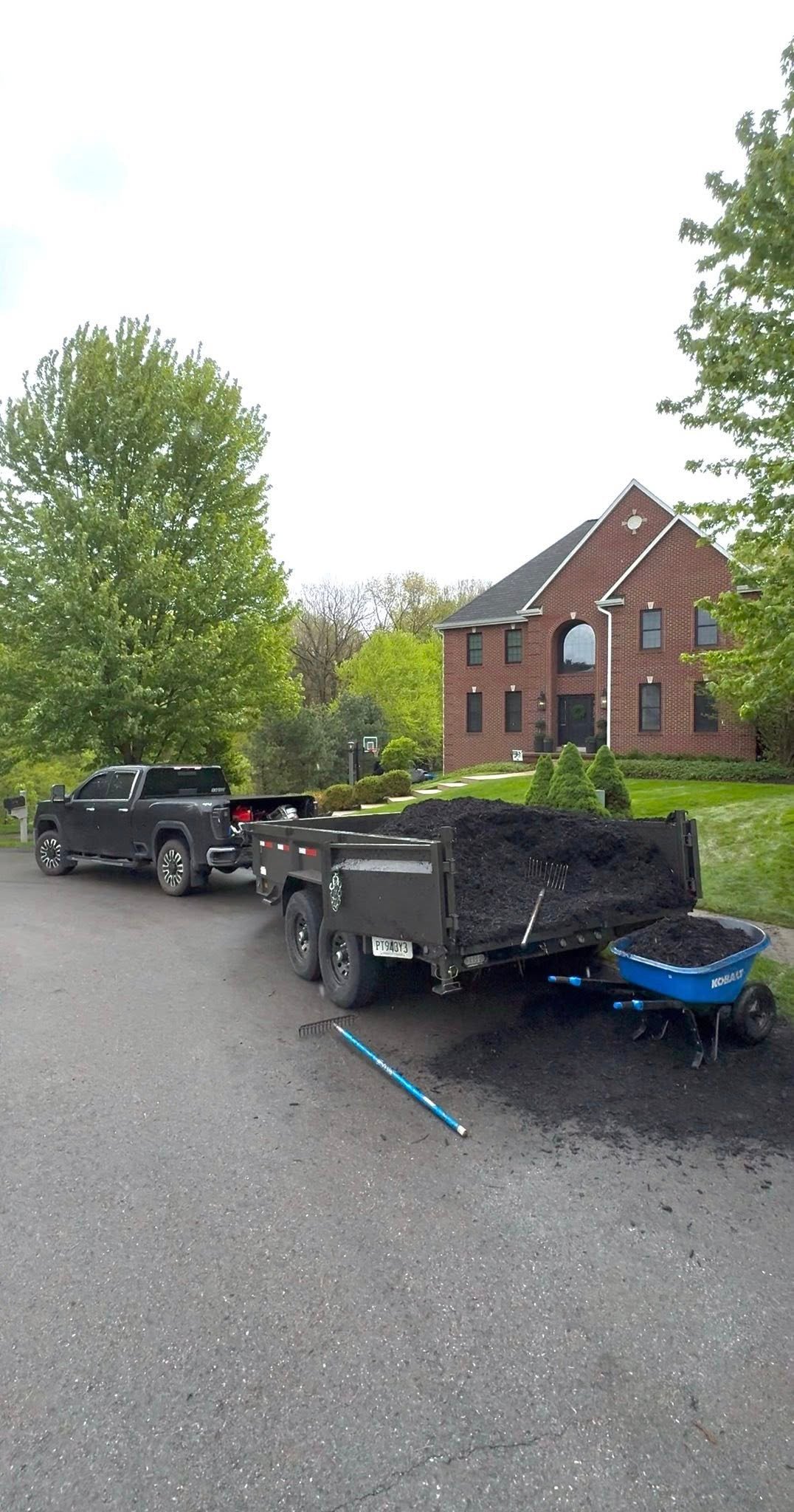 Black dump truck with trailer parked in driveway in front of two-story brick house with green lawn and trees